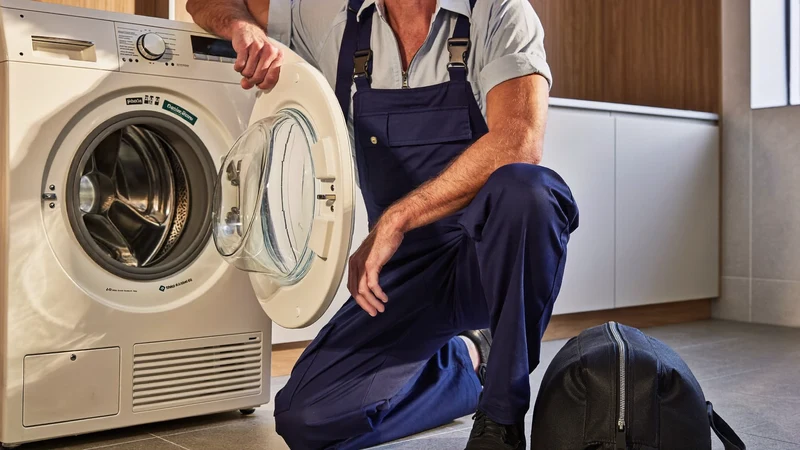 Technik klečí u otevřené pračky v domácí prádelně při denním světle